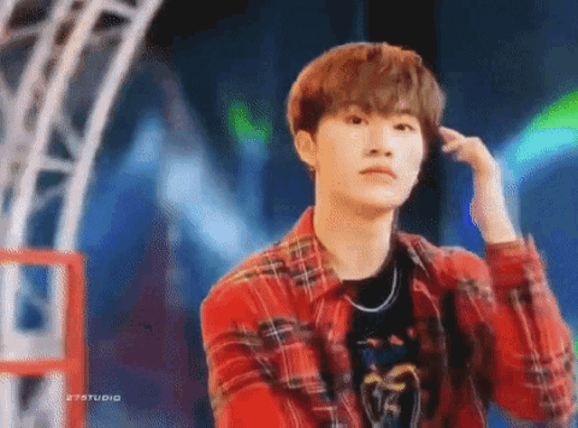 a young man in a red plaid shirt is standing on a stage and looking at the camera .
