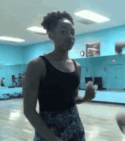 a woman in a black tank top is standing in a dance studio .