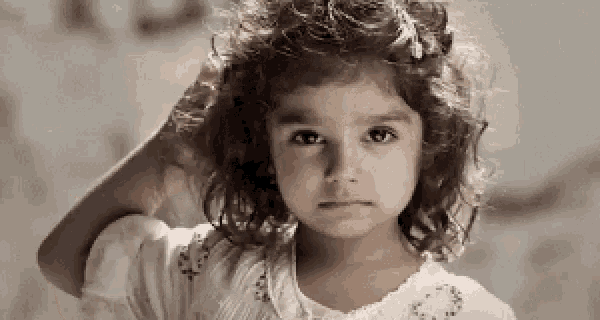 a little girl with curly hair is scratching her head with her hand .