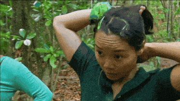 a woman in a green shirt adjusts her hair