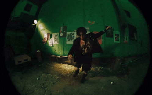 a fisheye shot of a man in a room with posters on the wall including one that says ' a ' on it