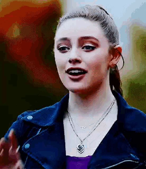 a woman wearing a blue jacket and a necklace is standing in front of a tree .