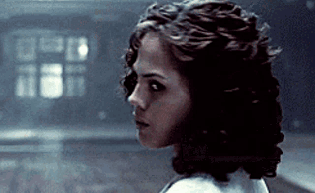 a woman with curly hair is standing in a dark room looking at the camera