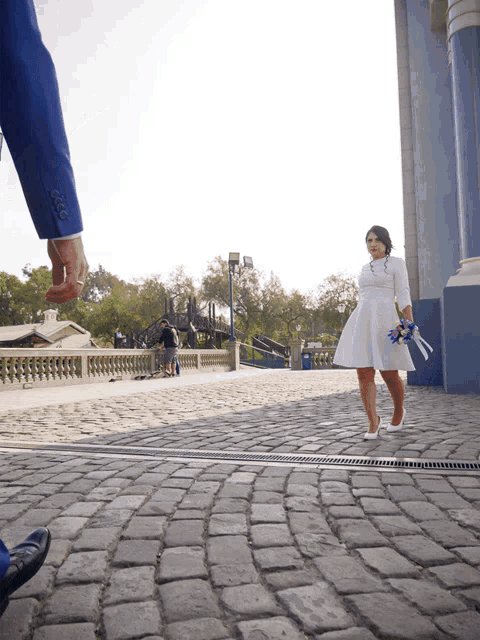 a man in a blue suit holds a woman 's hand as she walks down a cobblestone street