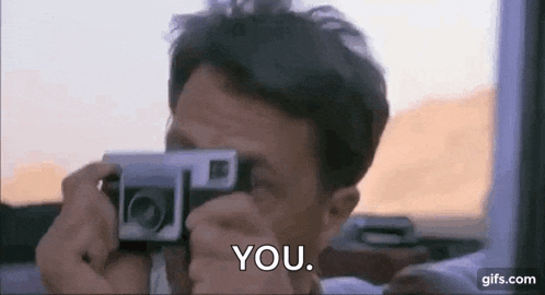 a man is taking a picture with a camera and says `` you '' in the background .