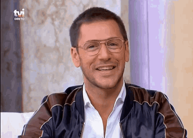 a man wearing glasses is smiling in front of a tv logo