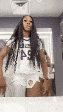 a woman with long hair is standing in front of a mirror wearing shorts and a white shirt .
