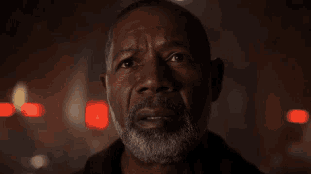a man with a beard looks at the camera in a dark room