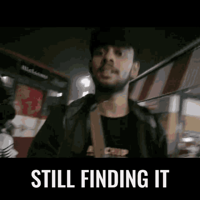 a man with a beard is standing in front of a bus with the words still finding it above him .