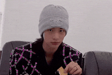 a young man wearing a chanel hat is sitting on a couch eating a snack