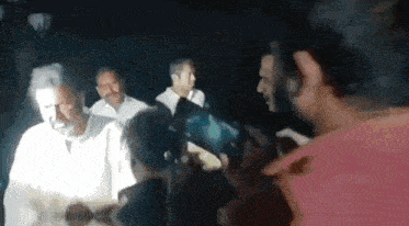 a man in a pink shirt is taking a picture of a man in a white shirt in a dark room .