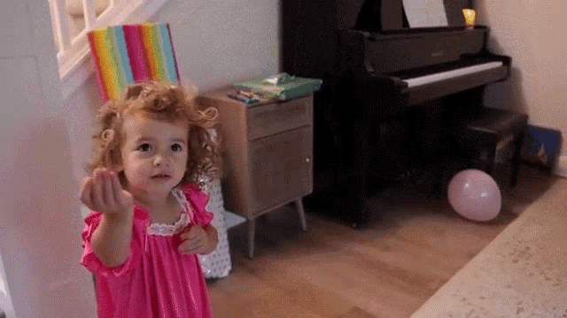 a little girl in a pink dress is standing in front of a piano and a pink balloon