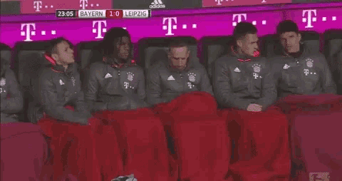 a group of soccer players sitting in a dugout covered in blankets