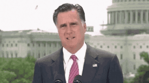 a man in a suit and tie is giving a speech in front of a microphone .