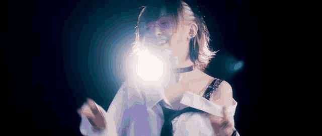 a woman in a white shirt and tie is dancing in a dark room with a light shining on her face .