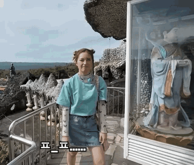 a woman in a blue shirt stands in front of a statue of a woman