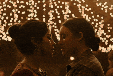 a couple of women kissing in front of a string of lights