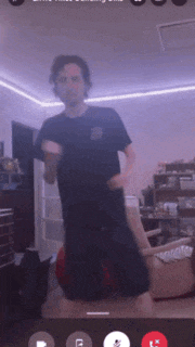 a man in a black shirt is dancing in a living room with purple lights