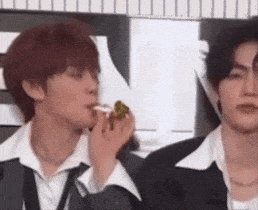 a man in a suit and tie is eating a sandwich while another man looks on .