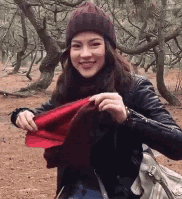 a woman wearing a purple hat and a black jacket is holding a red scarf in her hand .