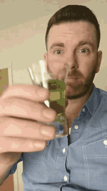 a man in a blue shirt is holding a shot glass with green liquid in it