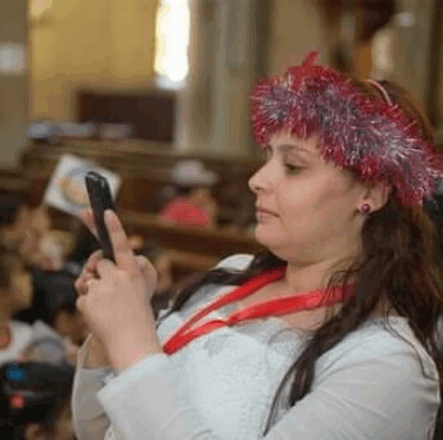 a woman wearing a red tinsel headband is holding a cell phone in her hand .