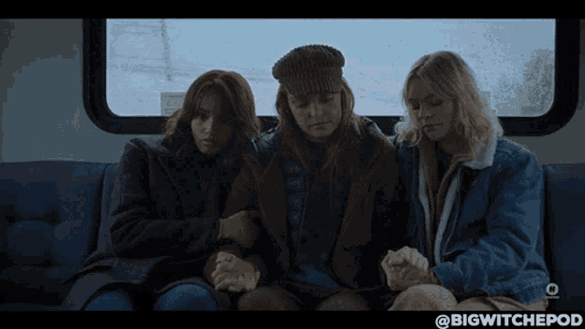 three women are sitting on a couch with their hands folded in front of a window with a sign that says exit