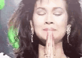 a woman with her eyes closed is praying with her hands together .