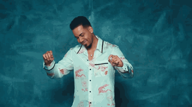 a man in a white shirt with dragons on it is dancing in front of a blue wall