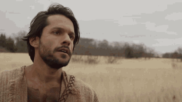 a man with a beard is standing in a field looking to the side