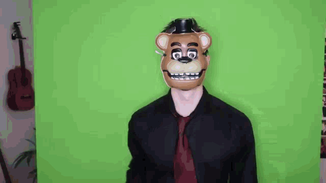 a man in a black shirt and red tie is wearing a teddy bear mask on his head .