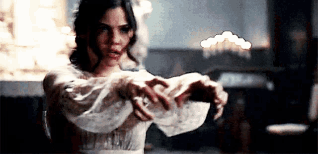 a woman in a white dress is making a heart shape with her hands in a dark room .