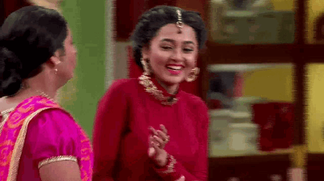 a woman in a red top is smiling while standing next to another woman in a pink sari .