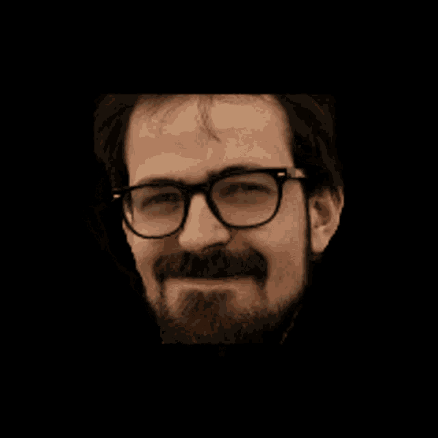 a man with glasses and a beard is smiling in the dark