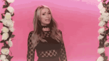 a woman in a black dress is standing in front of a pink background with flowers .
