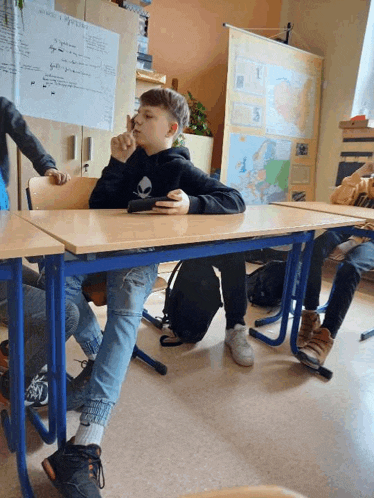 a boy in an alien shirt sits at a desk in front of a map