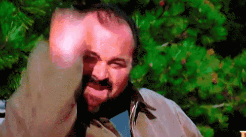 a man with a beard is making a funny face while standing in front of trees .