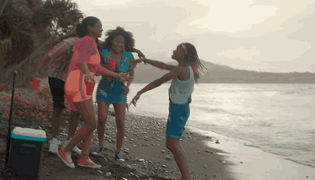 a group of people dancing on a beach with a cooler in the background