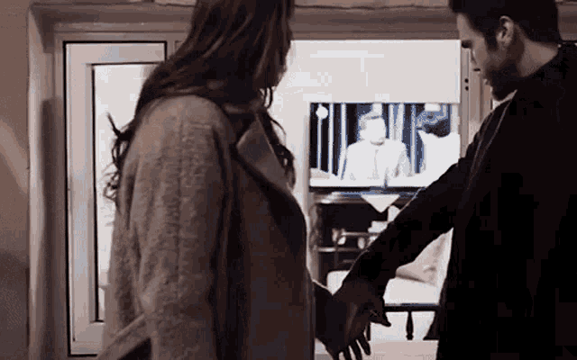 a man and a woman are holding hands in front of a television in a living room .