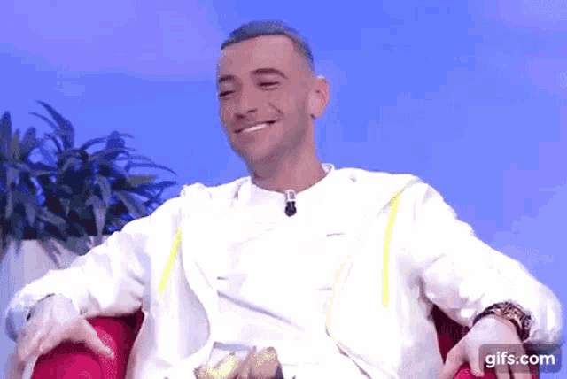a man in a white shirt is sitting in a red chair and smiling ..