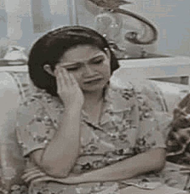 a woman is sitting on a couch with her hands on her face and crying .