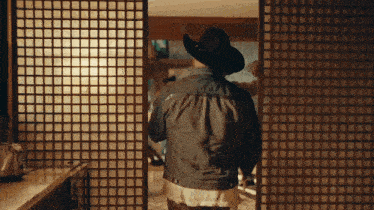 a man wearing a cowboy hat and a denim jacket walking through a room