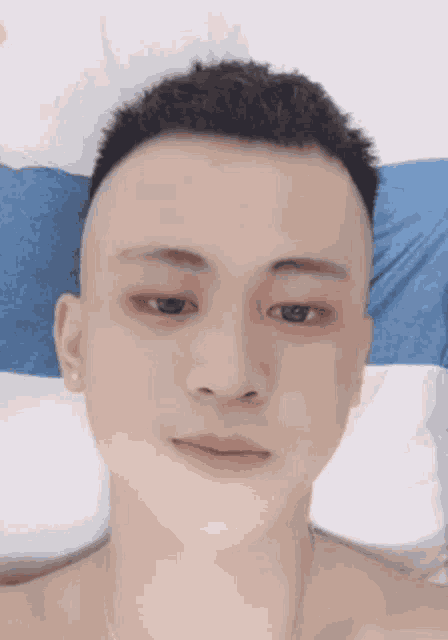 a young man without a shirt is laying on a bed with a blue and white pillow .