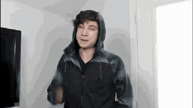 a young man wearing a hoodie and a black shirt is standing in front of a door .