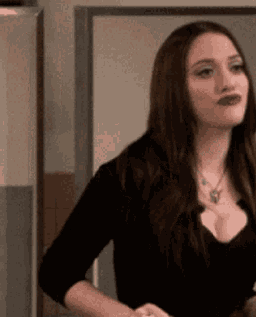 a woman in a black top with a necklace around her neck is standing in front of a door