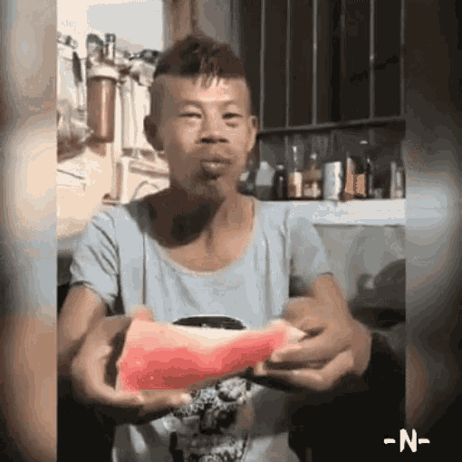 a man is eating a slice of watermelon with the letter n visible