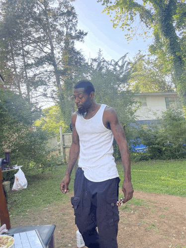 a man in a white tank top and black pants is standing in a yard