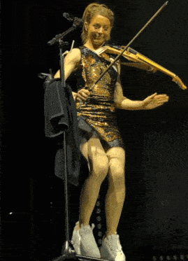 a woman in a sequined dress is standing on a stage holding a drum stick