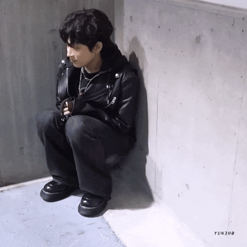 a man in a leather jacket is sitting on a wall with yun3ho written below him