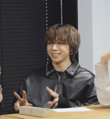 a young man wearing a black leather jacket is sitting at a table and smiling